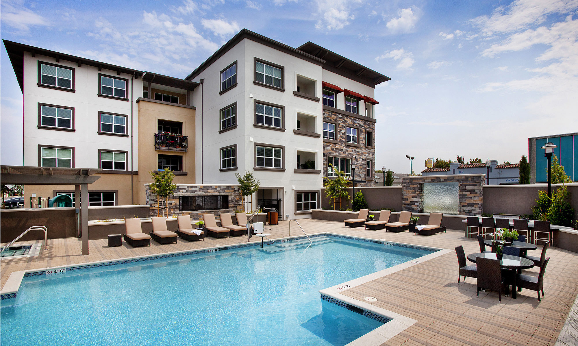 Pool with jacuzzi in the distance and seating all around. With view of units and balconies.